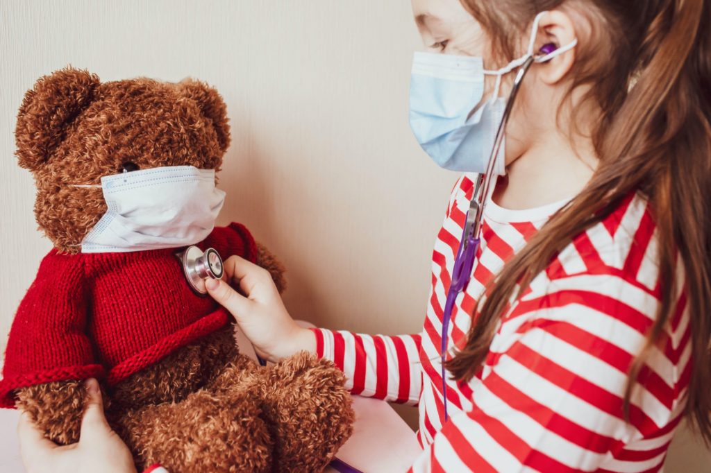 The girl plays at the doctor and examines the patient. Girl and soft toy bear in medical masks.